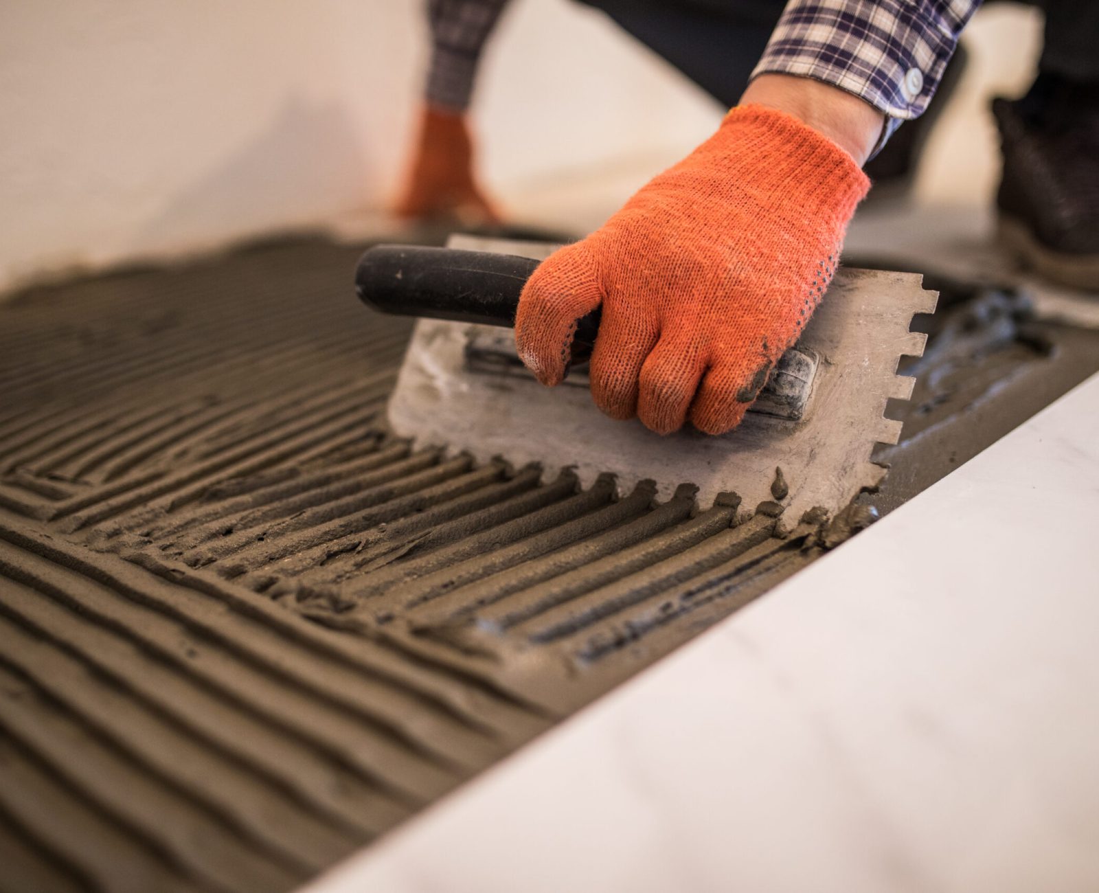Troweling mortar onto a concrete floor in preparation for laying white floor tile.