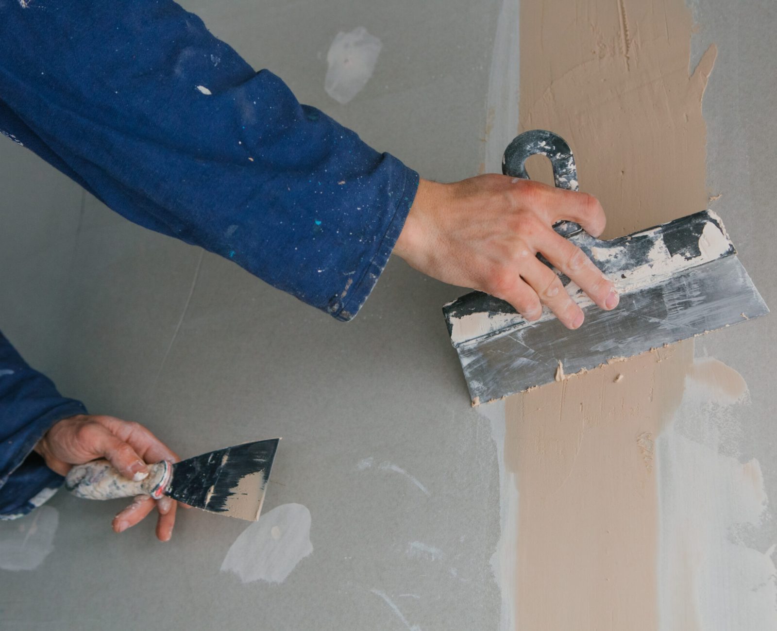 plasterer man works plastering two trowels on plasterboard in blue uniform