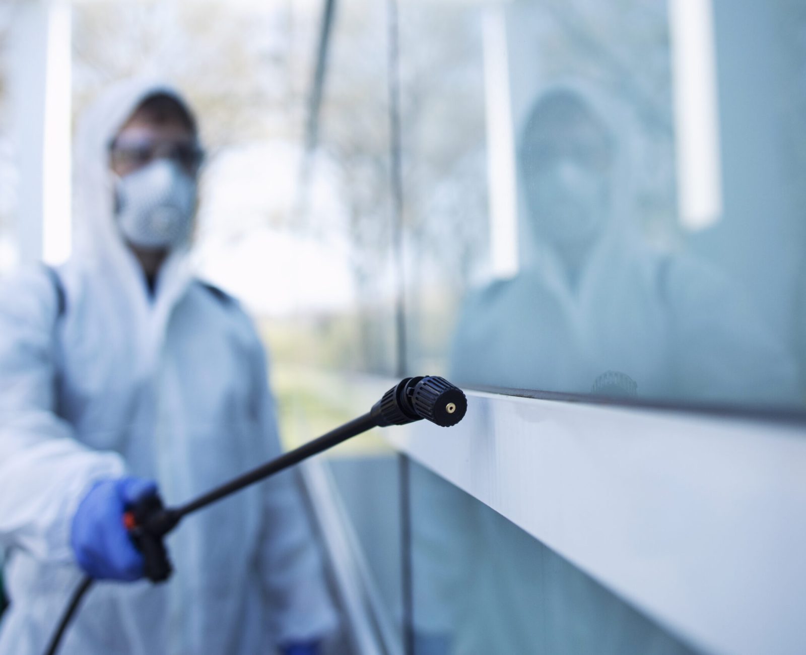 Person in white chemical protection suit doing disinfection of public areas to stop spreading highly contagious corona virus.